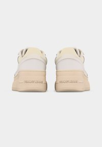 Paire de baskets blanches et beiges vues de dos, avec des semelles épaisses et "TOMMY JEANS" embossé sur la zone du talon.