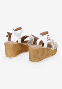 Sandalias de cuña blancas con detalle textil trenzado en la parte frontal, correa ajustable con hebilla y suela de goma marrón texturizada.