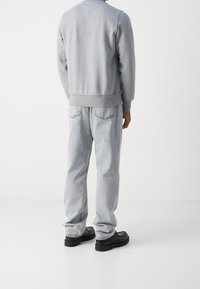 Sudadera gris con dobladillo y puños acanalados, combinada con jeans gris claro que cuentan con bolsillos traseros. Zapatos negros completan el conjunto.