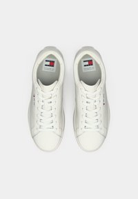 Sneakers in pelle bianca con texture liscia, punta rotonda e lacci. Presentano un'etichetta con logo sulla linguetta e un design minimalista.