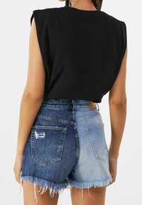 Top nero senza maniche e pantaloncini di jeans blu con orlo sfrangiato. I pantaloncini presentano un design bicolore con effetti di usura sulle tasche posteriori.