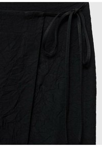 Tejido negro texturizado con un aspecto arrugado. Presenta una cinturilla atada y detalles de pliegues en el lateral.