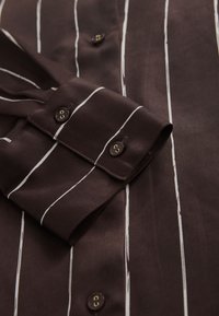 Braun gestreiftes Hemd mit glatter Textur, weißen vertikalen Streifen, geknöpften Manschetten und braunen Knöpfen mit goldenen Akzenten.