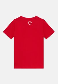 Raudona medvilninė marškinė su trumpomis rankovėmis, su balta Nike logotipu, esantį šarvo kontūre ant viršutinės nugaros dalies. Standartinis apvalaus iškirpimo dizainas.