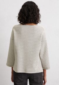 White and black striped pullover, lightweight fabric, three-quarter sleeves, round neckline, relaxed fit, visible texture from ribbed material.