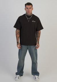 Sort kortærmet t-shirt med logo på fronten, parret med lyseblå løstsiddende jeans og hvide sneakers, som viser en afslappet pasform.