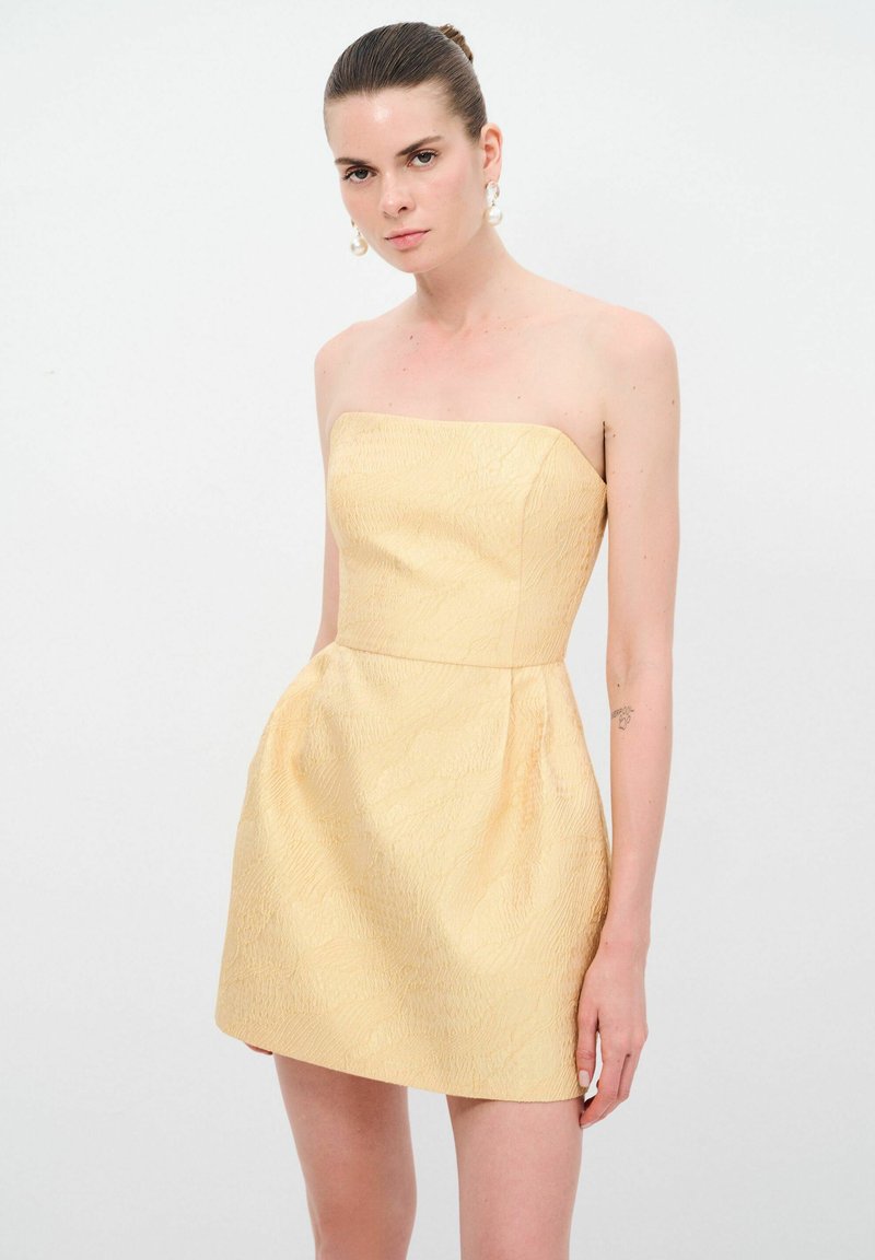 Gelbes trägerloses Kleid aus strukturiertem Stoff, tailliertem Oberteil und ausgestelltem Rock. Das Design weist ein dezentes Muster und eine glatte Oberfläche auf.