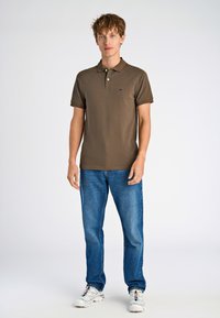 Ruskopärane polo särk lühikeste varrukatega, kahe nööbiga nööbirea ja väikese logoga. Sobitatud siniste teksade ja valgete spordijalatsitega.