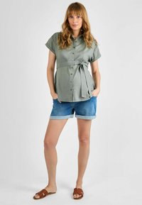 Hele roheline lühikeste varrukatega nööpidega särk, millel on seotud vöö, koos pööratud äärtega denim lühikesed püksid ja pruunid libisemisega sandaalid. Sile kangast tekstuur.