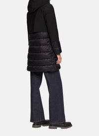 Zwarte pufferjack met capuchon, met een aansluitende bovenkant en een doorgestikte onderkant. Gecombineerd met donkere flared jeans en stevige zwarte laarzen.