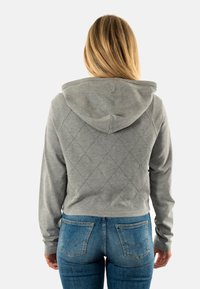 Hoodie gris coupé avec un motif matelassé en losanges au dos, doté d'une capuche et de poignets côtelés, associé à un jean en denim bleu.