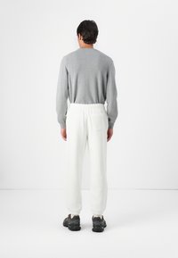 Grijze trui, witte joggingbroek met elastische tailleband en achterzak, gecombineerd met zwarte sneakers. Eenvoudige, casual outfit gezien van achteren.