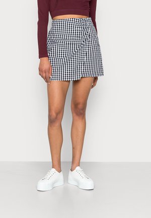 Musta ja valkoinen ruudullinen hame, jossa on rypistetty muotoilu ja epäsymmetrinen helma, yhdistettynä valkoisiin platform-kenkiin.