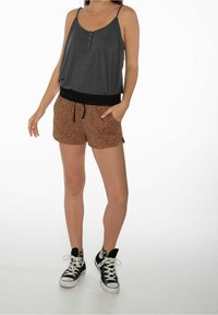 Top grigio senza maniche con bottoni abbinato a pantaloni corti arancioni a fantasia con una cintura elastica nera e cordoncino. Sneakers nere.