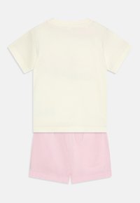 T-shirt giallo chiaro a maniche corte abbinata a pantaloni corti rosa tenue, entrambi realizzati in cotone con una texture morbida e un design semplice.