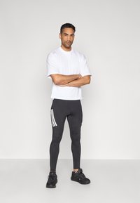 Herridrottskläder med en vit kortärmad tröja och svarta leggings med vita ränder, kombinerat med svarta sneakers.