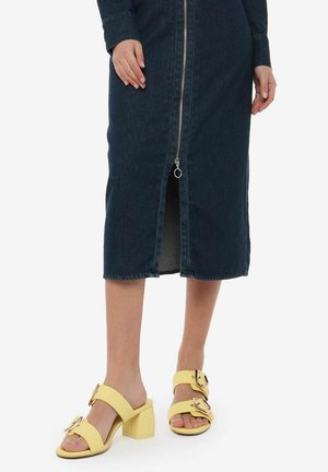 Donkerblauwe denim midi-jurk met een rits aan de voorkant en een split. Draagt het met gele platformsandalen met grote gespen.