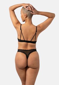 Zwart kanten lingerieset met een bralette met verstelbare bandjes en een string met gegolfde randen, die transparante en gestructureerde elementen benadrukt.
