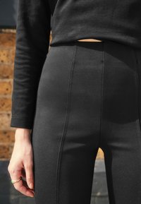 High-waisted black leggings with a smooth texture, featuring subtle side seams. Paired with a fitted black long-sleeve top.