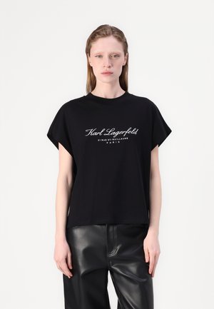 Musta lyhythihainen t-paita, jossa on valkoiset tekstit "Karl Lagerfeld 21 RUE ST.-GUILLAUME PARIS". Pehmeä materiaali, rento istuvuus ja pyöreä kaula-aukko.