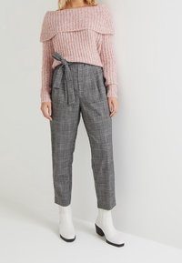 Maglione rosa lavorato a maglia con design off-shoulder, abbinato a pantaloni a quadri neri e bianchi a vita alta e stivaletti bianchi con tacco a blocco.