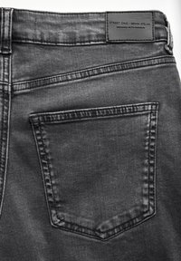 Jeans en denim noir avec une poche arrière unique, des détails de couture subtils et une étiquette de marque en cuir à la taille.