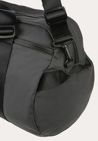 Borsa da viaggio nera con esterno liscio e impermeabile, dotata di tasca con cerniera, tracolla regolabile e manico laterale.