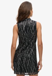 Robe noire sans manches avec un col haut, présentant un motif de sequins scintillants en argent et en or, avec une silhouette ajustée.
