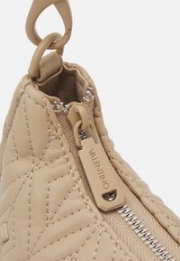 Beige quilted leather bag with a prominent zipper closure. Features a textured surface and branded zipper pull with “Valentino” engraving.