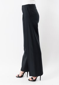 Pantaloni neri a gamba larga con una texture liscia, fronte plissè e vestibilità su misura. Indossati con sandali neri con tacco alto.