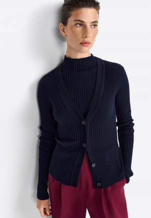 Marineblauwe geribbelde cardigan met een V-hals, knopenlijst aan de voorkant, lange mouwen en een gestructureerde gebreide stof, gecombineerd met een hooghals-top en een broek met wijde benen.