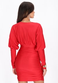 Rode jurk met lange, opgeblazen mouwen en een getailleerd, gerimpeld ontwerp. Gladde stoftextuur met een cinched taille en een subtiele glans.