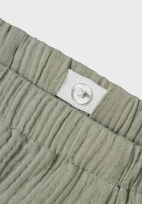 Tessuto verde chiaro strutturato con un design a plissé e un bottone bianco visibile in vita.