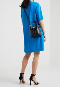 Sort lærspandtaske med rundt håndtag, sølvhardware og snorlukning, kombineret med en knaldbel blå kjole og sorte hælede sandaler.