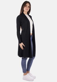 Cardigan lungo nero con una texture morbida, design aperto sul davanti e maniche lunghe, abbinato a una maglietta bianca e jeans blu.