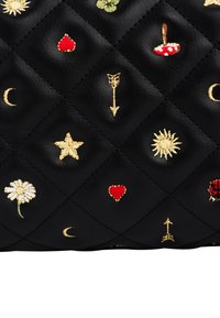 Superficie de cuero negro acolchado con bordados de estrellas doradas, flechas, lunas crecientes, corazones rojos, champiñones, margaritas, soles y una mariquita.