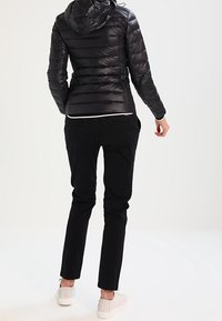 Zwarte gewatteerde jas met een capuchon, voorzien van horizontale quilting, gecombineerd met zwarte broeken en witte sneakers. Over het geheel een gladde, strakke textuur.
