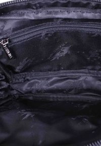 Intérieur en textile noir d'un sac avec une texture lisse, comportant un compartiment zippé et deux poches ouvertes supplémentaires pour l'organisation.