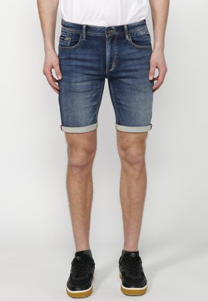 Denim shorts i mørkeblå vask, med oprollede manchetter, fem-lomme design, med syede detaljer, parret med sorte sneakers.