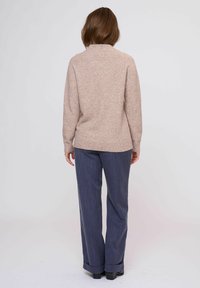 Maglione beige a maglia con colletto alto, abbinato a pantaloni navy a righe sottili. Tessuto morbido e vestibilità rilassata, visto da dietro.