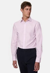 Camisa de manga larga de color rosa claro con cierre de botones, cuello regular y textura suave, combinada con pantalones oscuros en una pose de pie.