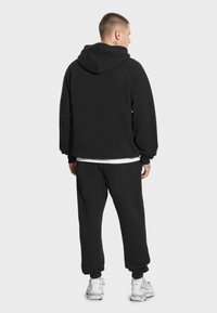 Czarna bluza z kapturem i spodnie dresowe wykonane z miękkiego materiału, z kapturem i elastycznymi ściągaczami, zestawione z białymi sneakersami. Prosty, jednolity design.