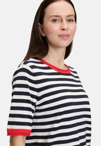 Stripet t-shirt med marineblå og hvide striber samt en rød ribbet krave og ærmeaccenter. Fremstillet af et blødt, letvægtigt stof.