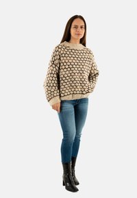 Maglione in maglia chunky color beige con motivo a pois multicolore, maniche larghe e polsini a coste. Abbinato a jeans skinny blu e stivali neri con tacco.