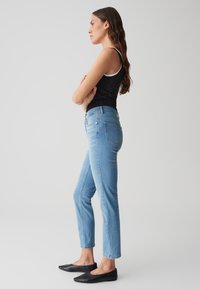 Jeans azzurri chiari a vita alta con una vestibilità slim, caratterizzati da un design a cinque tasche e una cucitura a contrasto. Indossati con un top nero senza maniche e ballerine nere.