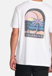 White cotton t-shirt featuring a colorful palm tree graphic, sunset, and "BILLABONG" text, with a relaxed fit.