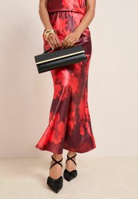 Punane lilleline satiinist kleit voolava disainiga, kombineeritud musta tekstuurse kättesahtliga, millel on kuldsed detailid ja musta paelaga kontsakingad.