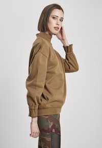 Sweatshirt maro cu guler înalt și mâneci supradimensionate, cu manșete cu nervuri, asortat cu colanți cu imprimeu militar. Textură netedă, design casual.