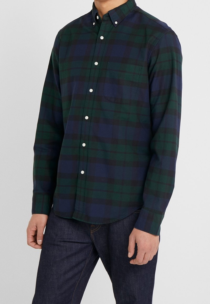 Camicia button-up in tartan verde scuro e blu navy. Presenta una tasca sul petto, bottoni bianchi e maniche lunghe. Il tessuto appare liscio e leggero.