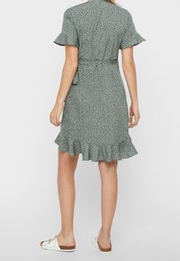 Zelené šaty s bílým květinovým potiskem, krátké rozšířené rukávy, pásek v pase a volánkový lem. V kombinaci s plochými sandály, texturovaná látka.